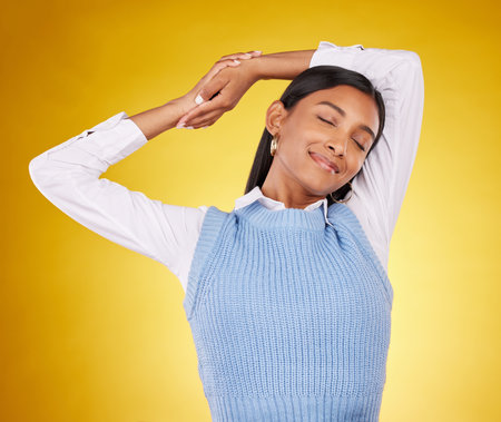 Relax, stretching and a woman on a yellow background in studio for peace, quiet or free time. Freedom, sleepy or lifestyle and an attractive young female posing with her eyes closed for a stretchの写真素材