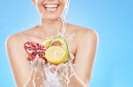 Cleaning, water and hands with fruit in studio on blue background for nutrition, natural and healthy lifestyle. Wellness, body care and woman with fruits and vegetables with water splash for dietの写真素材