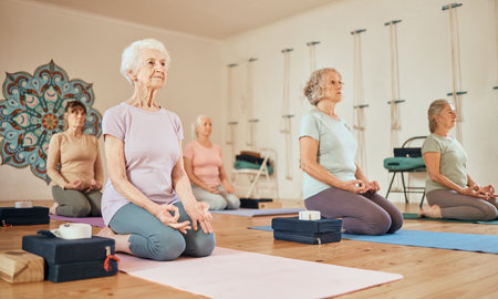 Yoga, lotus and group of senior women in gym meditating for spiritual health and wellness. Meditation, zen chakra and retired females training to relax for mindfulness and peace in fitness center.の写真素材