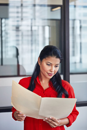 Business is booming. a casually dressed businesswoman reading through paperwork in the office.