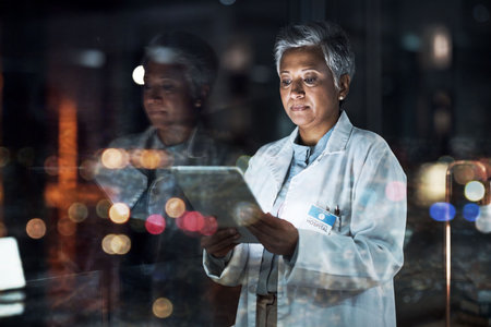 Medical, research and night with doctor and tablet for planning, medicine and schedule. Technology, review and digital with senior woman reading report for healthcare, science and life insurance newsの写真素材