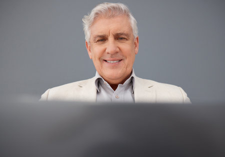 Senior, computer and professional business man isolated on a gray background for online planning and market research. Corporate person, boss or executive working on laptop tech for asset managementの写真素材