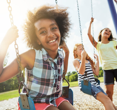 Having a cheerful time together. Portrait of a young girl playing on a swing at the park with her friends.の写真素材