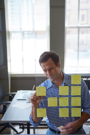 Strategic maneuvers are second nature to him. a handsome businessman arranging adhesive notes on a glass pane.の写真素材