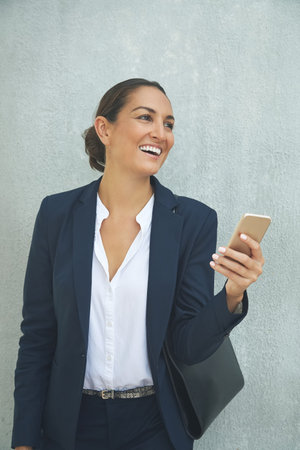 Success is just a call away. a young businesswoman using her phone while standing against a gray...