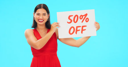 Sale sign, portrait and woman in studio advertising percentage or discount rate on paper or banner. Smile of a happy female on a blue background for fashion promotion deal, savings or deal and offerの写真素材