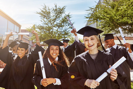 Ready for the world with diploma in hand. Portrait of a group of smiling university students outside on graduation day.の写真素材