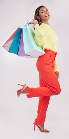 Portrait, retail and sale with a woman customer in studio on a gray background for shopping or consumerism. Fashion, luxury or happy with a female consumer or shopper carrying bags on her shoulderの写真素材