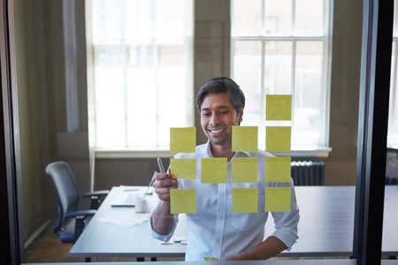 One part traditionalist, one part groundbreaker. a handsome businessman arranging adhesive notes on a glass pane.の写真素材