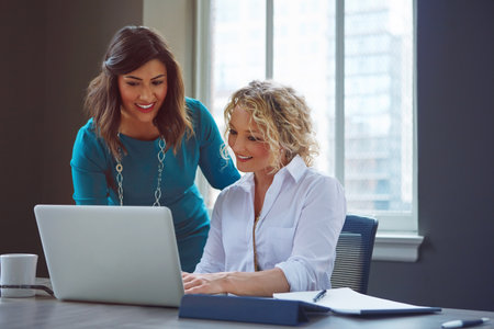 Teamwork is paramount to success. two businesswomen using a laptop together in an office.の写真素材