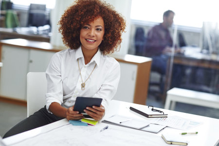 Now I can take my business on the go. a beautiful young businesswoman using her tablet in the office.の写真素材