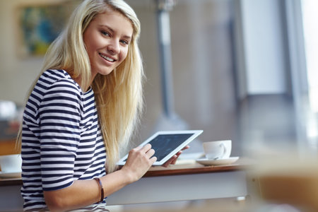 Staying connected. Portrait of a beautiful young woman sitting with her tablet in a coffee shop.の写真素材