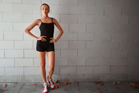 Lets get serious about health. Full length portrait of a sporty young woman standing with her hands on her hips against a wall.の写真素材