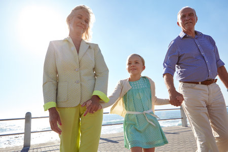Being a grandparent is the best feeling in the world. grandparents walking hand in hand with their granddaughter on a promanade.の写真素材