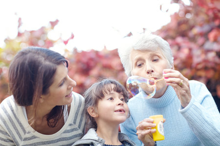 You will never regret time spent blowing bubbles. a three generational family spending time outdoors blowing bubbles.の写真素材