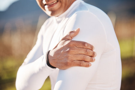 Hand, shoulder and injury with a runner man outdoor for cardio or endurance exercise in nature. Pain, arm and emergency with a male athlete suffering from cramp after an accident while runningの写真素材