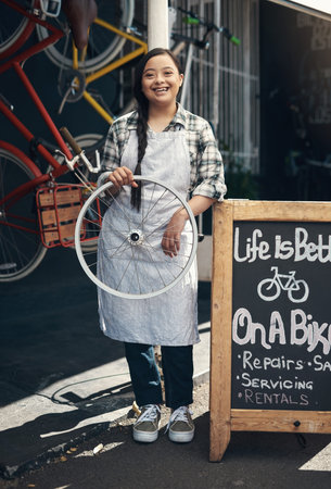 This is my birch tree. Portrait of a young woman holding a bicycle wheel outside of a bicycle repair shop.