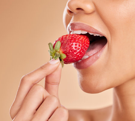 Healthy, eating and a woman taking a bite of a strawberry while isolated on a studio background. Health, organic and a girl tasting a fruit for nutrition, diet or hunger for a snack on a backdropの写真素材