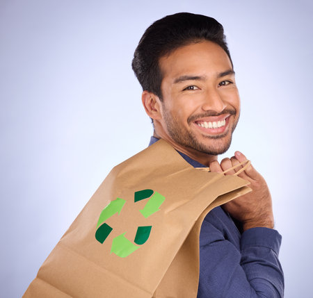 Man in portrait, happy and recycling paper bag, environment and sustainable shopping on studio background. Eco friendly, green and climate change awareness in retail, sustainability and recycle logoの写真素材