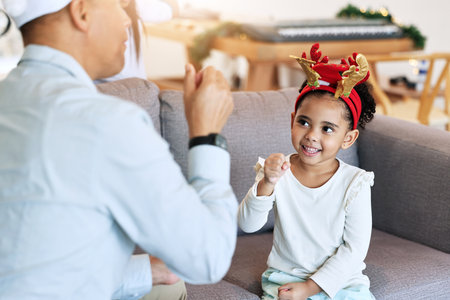 Christmas, girl and home holiday fun with a father and parent care on a living room sofa. Family, vacation bonding and happiness of a child and dad ready for celebration with party hats in a houseの写真素材
