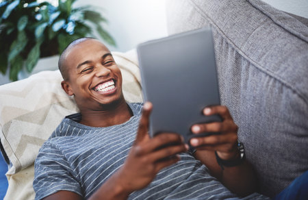 Theres no need to leave home to stay entertained. a handsome young man using a digital tablet at home.の写真素材