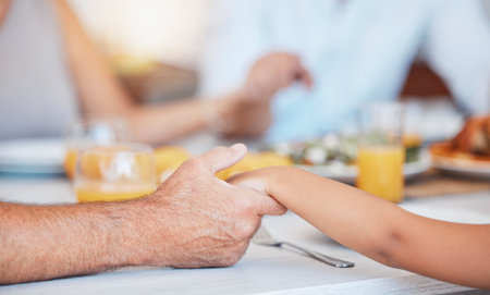 Family, hands and gratitude prayer for food at table together for faith, religion and appreciation. Christian, child and senior man holding hands to give thanks and pray to God for lunch.の写真素材