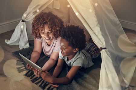 Black family, tablet and mother with kid in tent at night watching movie, video and having fun in home. Technology, bokeh and smile of happy African mom bonding with boy child while streaming filmの写真素材