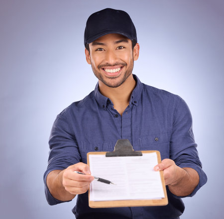Delivery, signature and portrait of Asian man with paperwork isolated on a studio background. Happy, showing and courier asking to sign a document for approval of a service, import or packageの写真素材