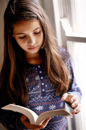 Today a reader tomorrow a leader. Portrait of a cute little girl reading at home.の写真素材