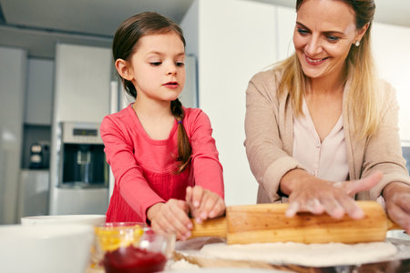 She is a natural. a middle aged mother and her daughter preparing a pizza to go into the oven in the kitchen at home.の写真素材