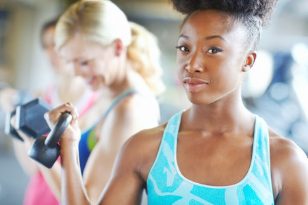 This thing is lighter than my bag. an attractive young woman holding a dumbbell in gym.の写真素材