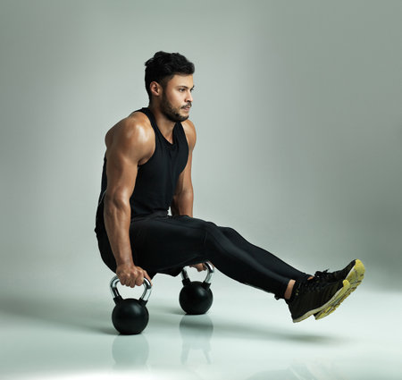 Working every part of his body. Studio shot of a young man working out with kettle bells against a gray background.の写真素材