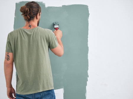 Painting, brush and renovation with a man doing interior DIY in a room for improvement and remodel of home. Young man, decoration and work with green paint on a wall to maintenance in domestic houseの写真素材