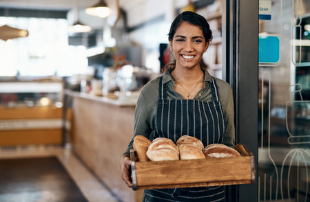Served fresh just for you. a young woman holding a selection of freshly baked breads in her bakery.の写真素材