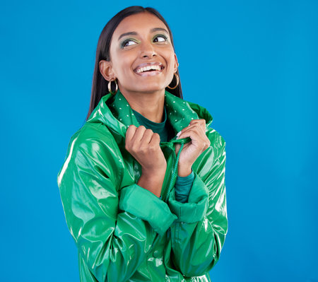 Gen z, Indian woman and fashion aesthetic of a young female in a isolated studio. Smile, happiness and raincoat for cold weather with blue background and person feeling happy from youth and styleの写真素材