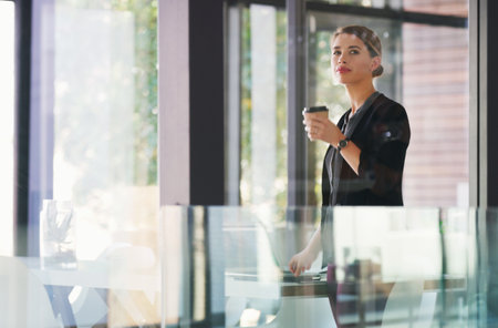 I really needed my coffee to get me through today. an attractive young businesswoman standing alone in her office and holding a cup of coffee.の写真素材