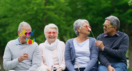 The golden years just got a whole lot more fun. a group of happy senior men and women wearing fun glasses at the park.の写真素材