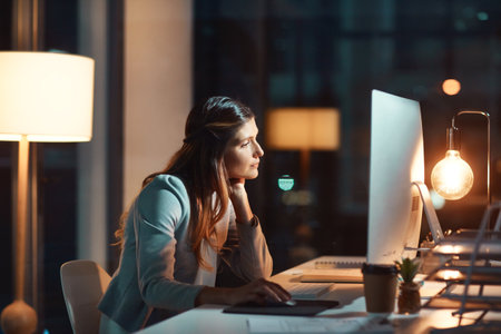 Making it happen no matter the time. a young businesswoman using a computer during a late night at work.の写真素材