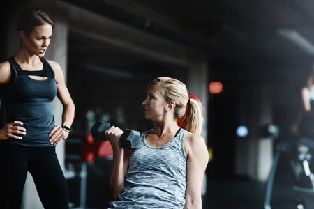 You doing a great job, keep it up. a mature woman lifting weights with a female instructor at the gym.の写真素材
