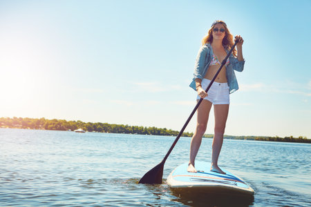 Let me take you on a paddle through my happy place. an attractive young woman paddle boarding on a lake.の写真素材