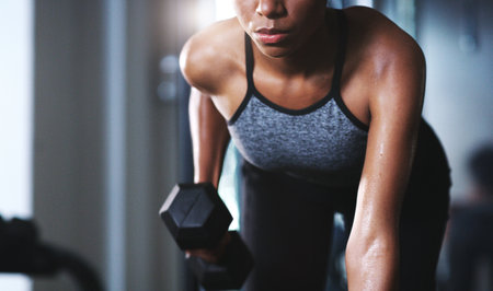 Dont wish for a good body, work for it. a sporty young woman exercising with a dumbbell at the gym.の写真素材