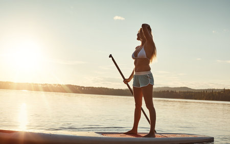 All I need is my board and sun. an attractive young woman paddle boarding on a lake.の写真素材