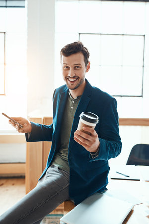 This is how I do business. Cropped portrait of a handsome young businessman using his cellphone while working in a modern office.の写真素材