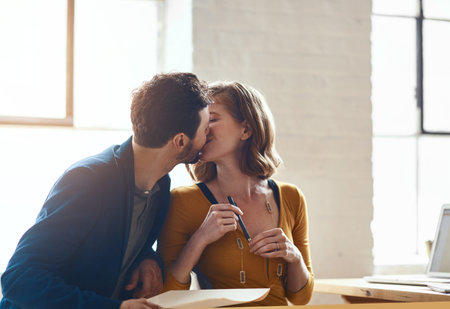 Working together has brought them closer. young couple kissing while working together in their...