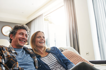 We love to laugh therefor we love watching comedies. a mature married couple relaxing on the sofa at home.の写真素材