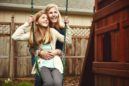 No one else makes me feel this happy. a mother and her daughter playing on a swing in their backyard.の写真素材