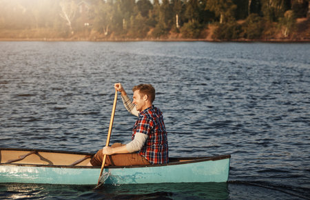 Hes on course for adventure. a young man rowing a boat out on the lake.