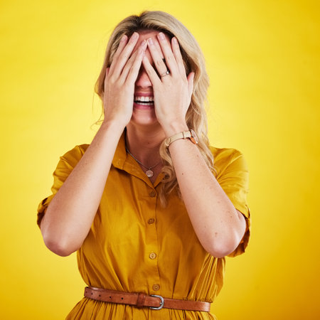 Comic, funny and embarrassed with a woman on a yellow background in studio laughing at a joke. Smile, comedy and humor with a person enjoying laughter or fun while covering her face in expressionの写真素材