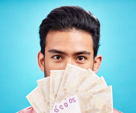 Man in portrait, money fan and cash with finance, prize or reward isolated on blue background. Financial savings, bonus or competition win with payment, male person with economic success in studioの写真素材