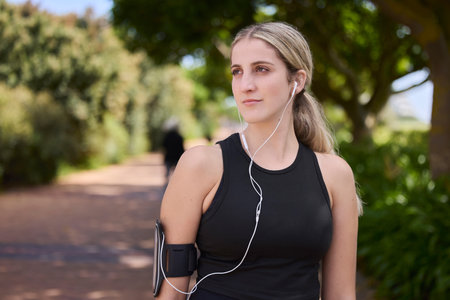Headphones, runner or woman thinking in park training, exercise or workout for a healthy body. Wellness, fitness break or sports girl athlete exercising or streaming audio or radio song in natureの写真素材